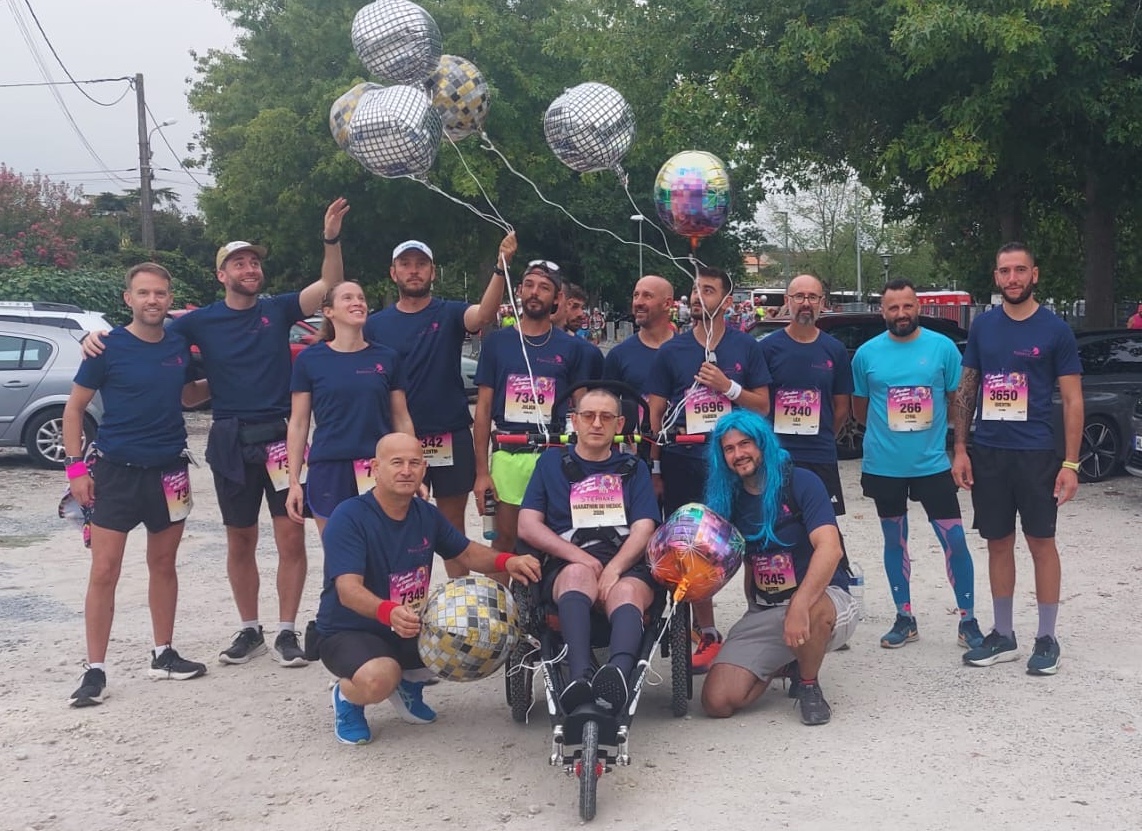 L'équipe de Château Pontet-Canet en tee-shirts floqués, avec ballons disco, autour de Stéphane Craviotto dans son fauteuil adapté et de Xavier Lacombe en perruque bleue, avant le départ du Marathon du Médoc